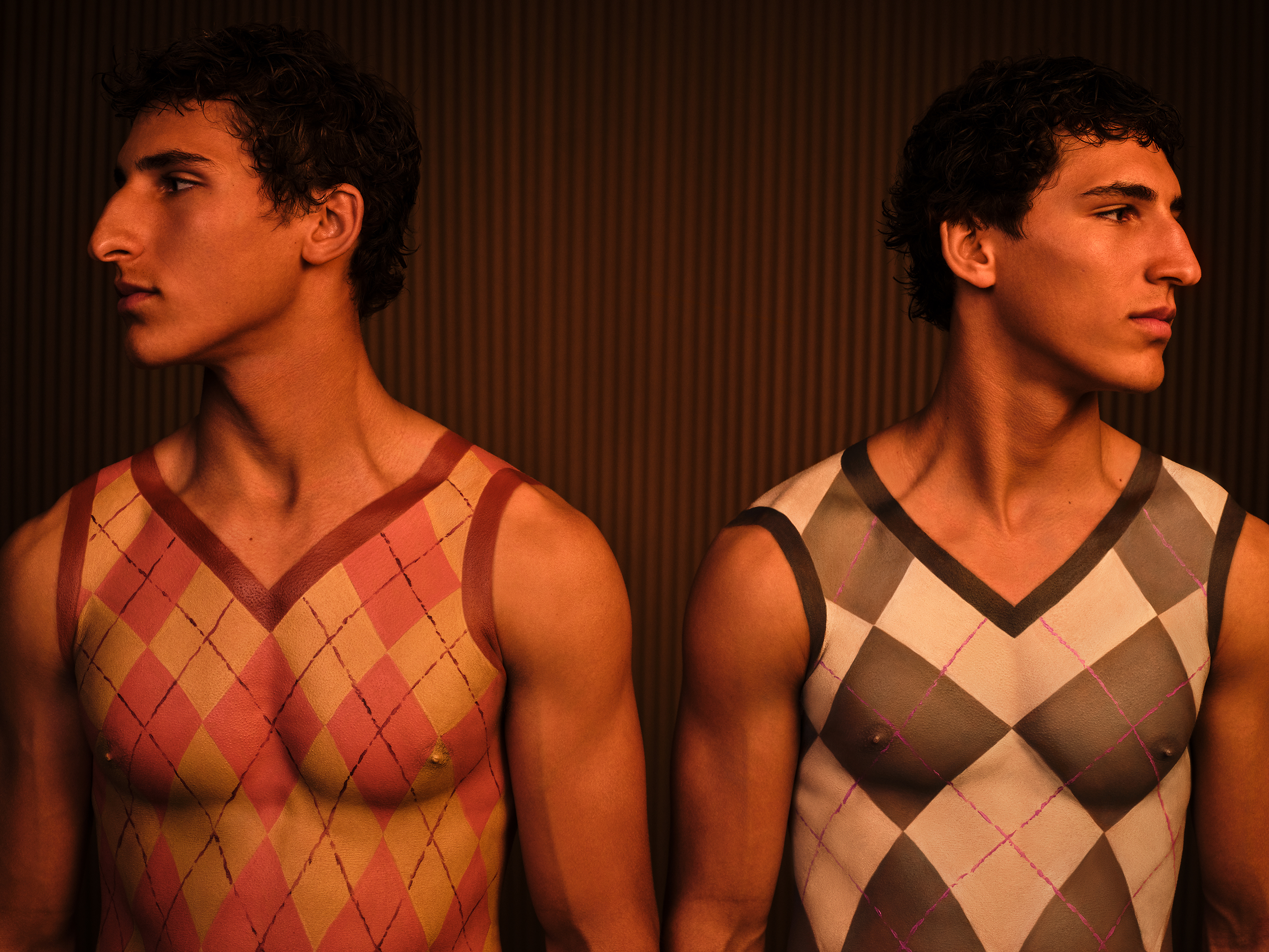Twin brothers both with body painted plaid sweater tops, looking opposite directions against a dark wood backdrop